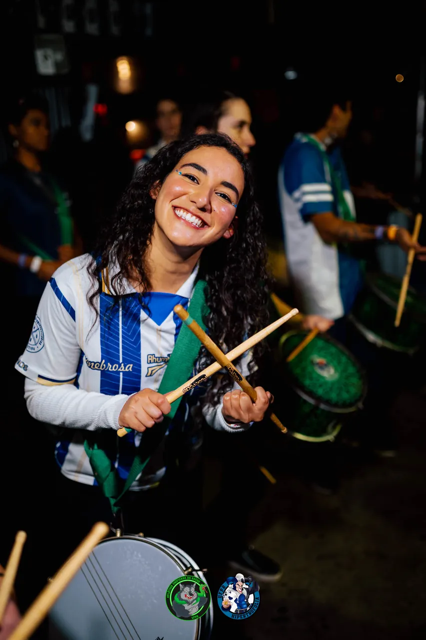 Ritmista da bateria da atlética tocando caixa com a camisa listrada