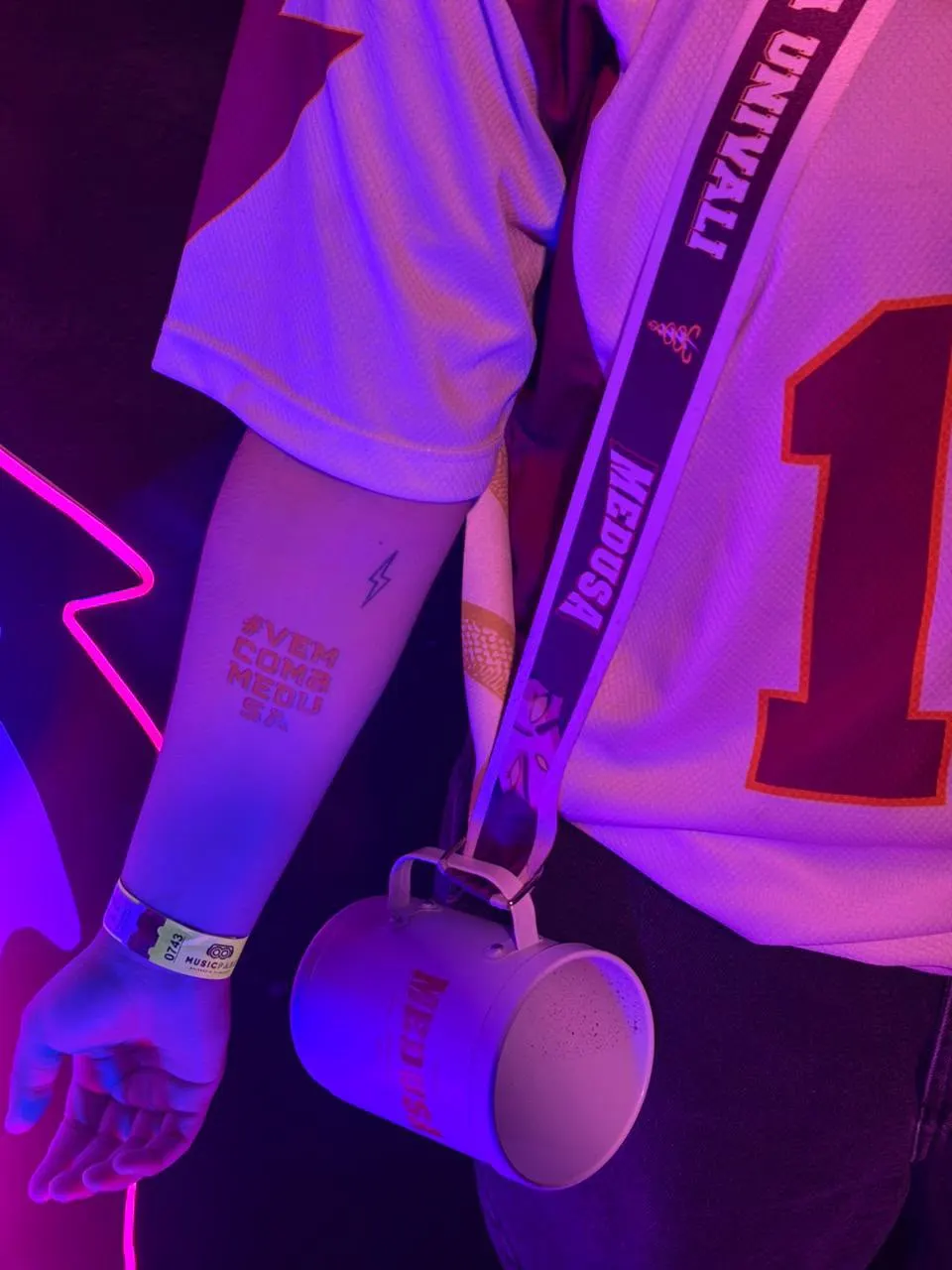 Caneca e tirante da atlética pendurados no ombro em festa com luz neon