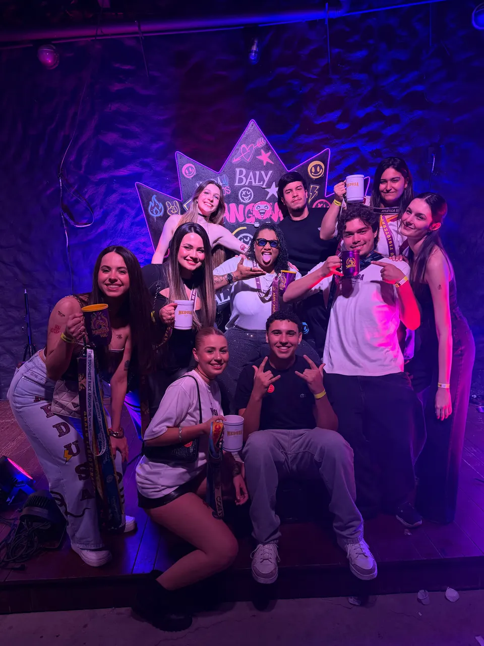 Galera da atlética posando no palco da festa com canecas personalizadas