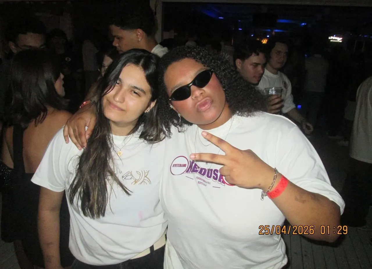Amigas com camisetas da atlética fazendo pose em festa universitária