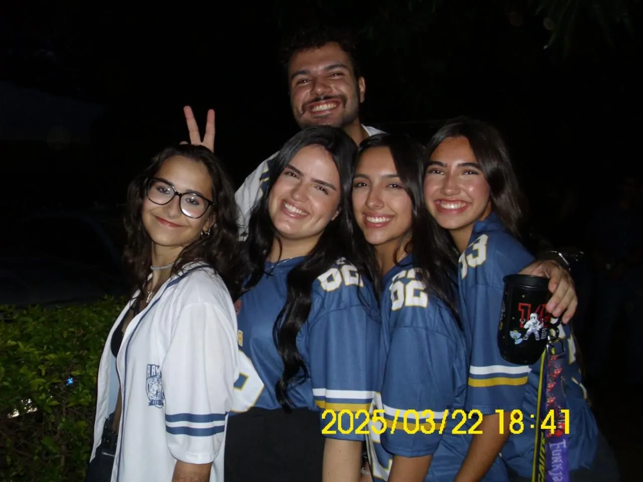 Amigos com camisas da atlética sorrindo juntos em evento à noite