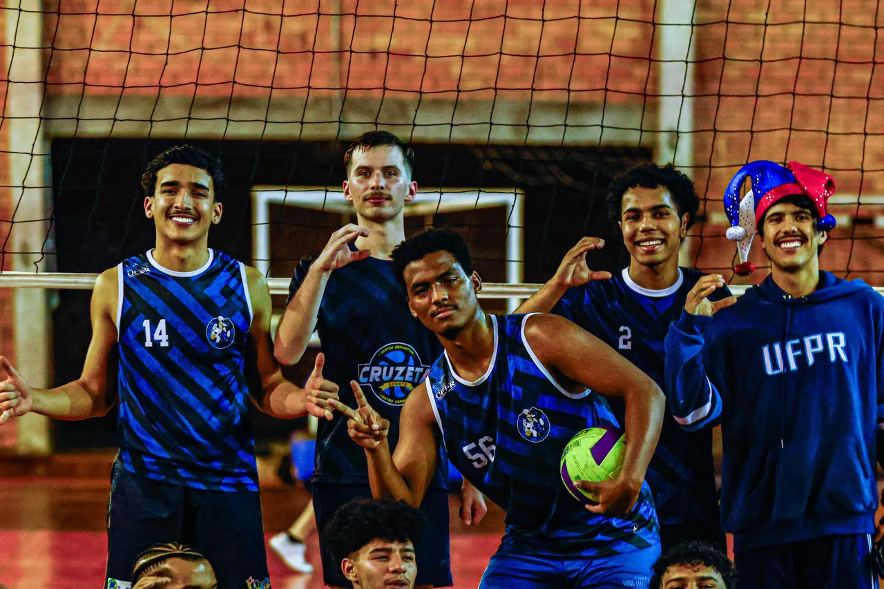 Time masculino de vôlei da atlética posando com a bola na quadra